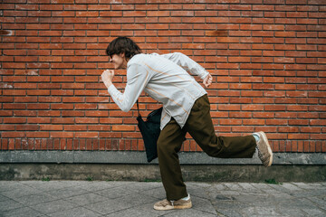 Fototapeta na wymiar Man pretending to run fast in front of brick wall, playful and humorous concept.