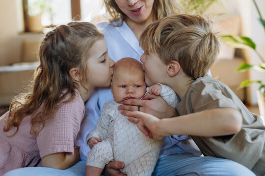 Siblings kissing the cheeks of a little baby. Big brother and big sister meeting newborn sister, enjoying together time.