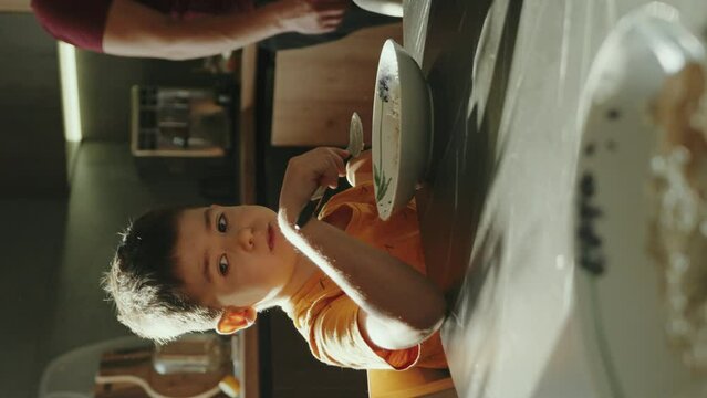 Young man in casual t-shirt eating breakfast in bowl sitting at table in light kitchen at home alone. Healthy diet lifestyle concept oking food in light kitchen
