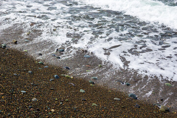 Foamy sea waves meeting a pebbled beach with colorful stones