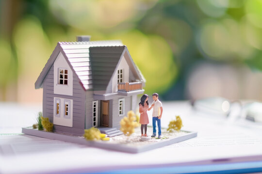 Figurine couple stand before a model house as they finalized the purchase