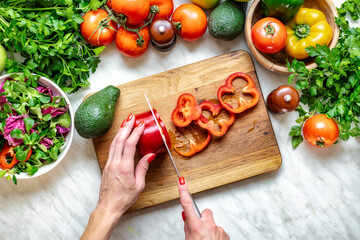 Healthy lifestyle concept. Female hands cut peppers for cooking a dietary summer salad at home in the kitchen, top view