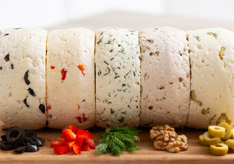 Closeup of Several varieties of homemade cheese with different fillings from paprika, herbs, olives and walnuts on a wooden board. - 755176162