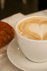 A cup of delicious morning coffee with a drawn heart and a croissant on the background. Selective soft focus - 755176329