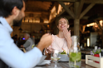 Happy loving couple at date in restaurant. Husband and wife sitting at table, laughing, having lunch in modern cafe. - 755176355