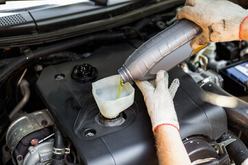 Changing the engine oil. A car mechanic pours oil from a bottle through a funnel into the engine...