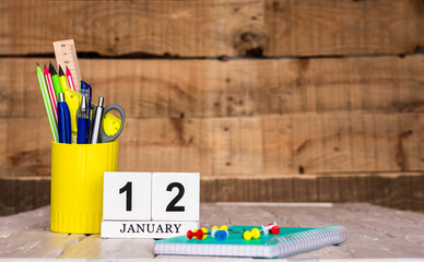 January calendar background with number  12. Stationery pens and pencils in a case on a wooden vintage background. Copy space notepad with pencils and a calendar. Planner place for text.