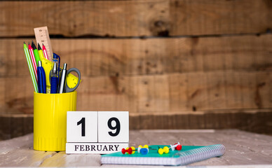 February calendar background with number  19. Stationery pens and pencils in a case on a wooden...