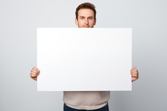 Mann hält weißes Schild mit Textfreiraum, Junger smarter Mann mit einem weißen leeren Schild für Werbung und Botschaften
