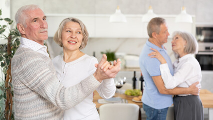 Couples of elderly women and men dancing in kitchen at home