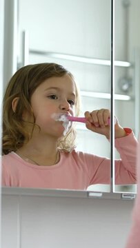 Little girl diligently brushing his teeth in the mirror. Close up