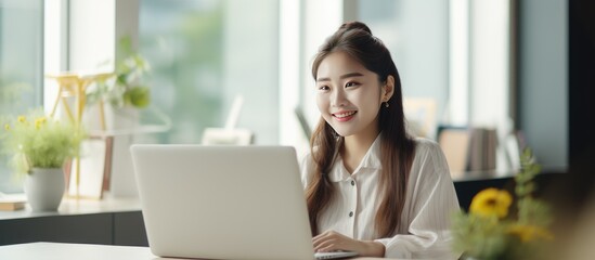 A smile Asian woman, entrepreneur of a small to medium-sized business, is sitting in her home office and working on her laptop. She appears focused and engaged in online marketing and managing SME