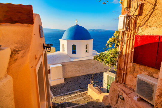 Fototapeta Oia village Image. Blue church and narrow street with yellow houses on Santorini island, Greece