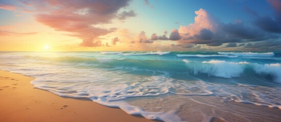 The azure sky is painted with streaks of pink and orange as the sun sets over the horizon. The waves crash onto the shore creating a beautiful natural landscape - obrazy, fototapety, plakaty