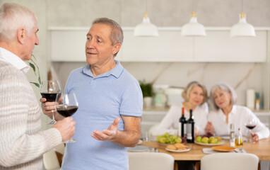 Fototapeta na wymiar Two elderly men friends chatting and drinking wine in kitchen at home