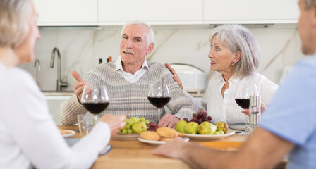 At the table, happy group of adults enjoy their holiday, drink red wine and talk together