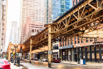 Low angle view of a train running on elevated tracks over a street lined with both modern high rises and traditional brick buildings in downtown Chicago