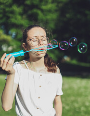 Portrait of a Caucasian teenage girl blowing soap bubbles in the park.