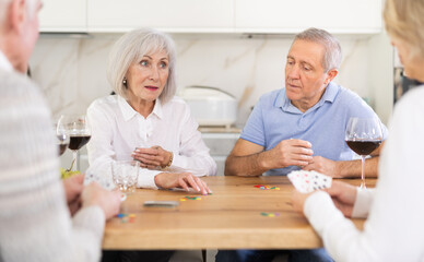 Obraz premium Senior men and women play card game poker during friendly gatherings at home. Couple enthusiastically participate in game, believe in luck, collect chips, distribute winnings