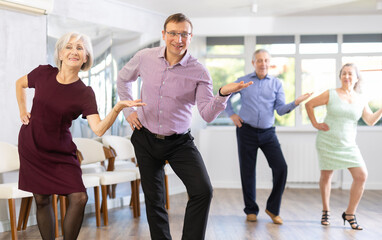 Middle-aged man and elderly woman are dancing contemporary twist in couple during lesson at studio....