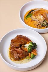 Two plates with meat dishes and mashed potatoes angle view on beige background