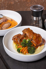 Plate of beef ribs in barbecue sauce with vegetables and mashed potatoes on dark table