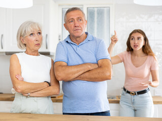 Adult daughter scolds elderly parents, mom and dad, in a modern kitchen