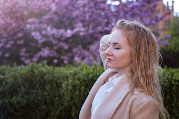 Attractive young woman with closed eyes and red hair in blooming spring park. Cherry blossom tree background. Side view.