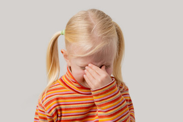 Tired little blonde girl covered her nose with her hand. Isolated on a gray background.