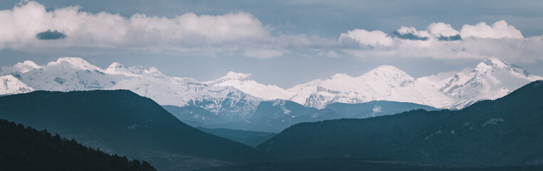 Fototapeta na wymiar Panoramic photograph of the Pyrenees in winter. Snow-capped peaks with clouds on the horizon. View of the mountain range from Navarra, Spain. Roncal Valley.