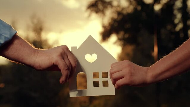 Paper house hands family, sun shines in window close-up. Hands, paper house at sunset. Symbol home, family comfort, happy. Concept building house family, child. Dream buy house. Real estate insurance