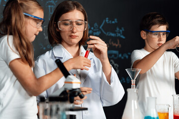 Teacher in support and watch student in laboratory they wear safety glasses, stand and experiment about science of chemistry in STEM class. Student funny do experiment with liquid in tube. Erudition.