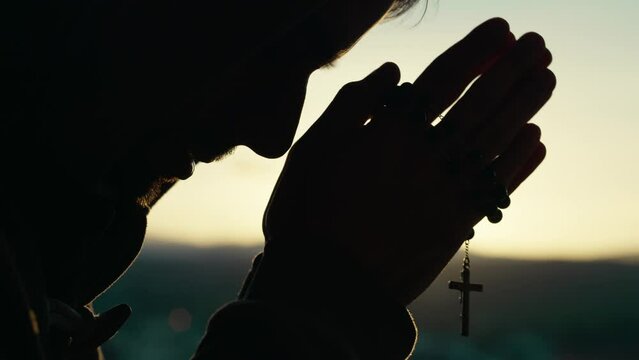 Man prays at sunset with rosary
