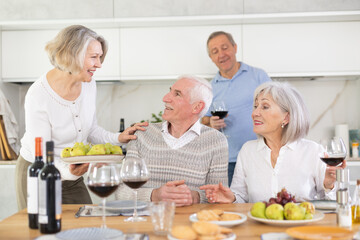 Group of happy elderly people drink red wine and chat at festive table. High quality photo