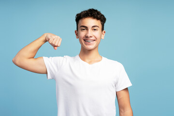 Portrait smiling strong teenage boy wearing stylish white t shirt showing muscles looking at camera