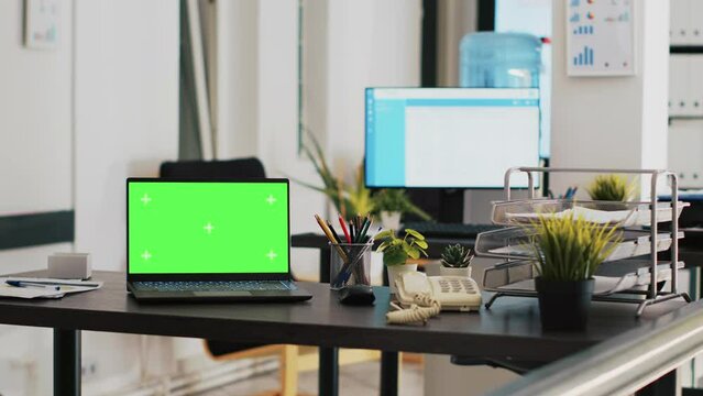 Office with green screen laptop and display in background with scheduled clients list. Mockup notebook in workspace and customers financial consultations list in the back on monitor