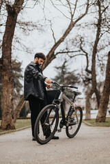 A business entrepreneur stops on a pathway to check his mobile phone, standing beside his mountain bike in an urban park setting.