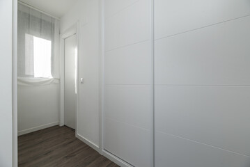 Dressing room in a bedroom with white sliding door closets in a hallway with a window and access to a small bathroom.