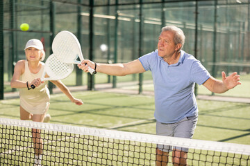 Dynamic old man and woman playing Padel Tennis with partners in the open air tennis court - obrazy, fototapety, plakaty