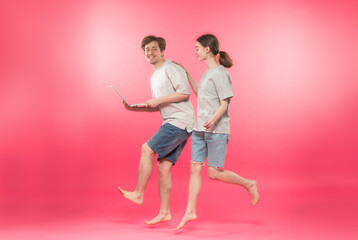 a couple of happy young people, students running with a laptop in full growth on a pink background