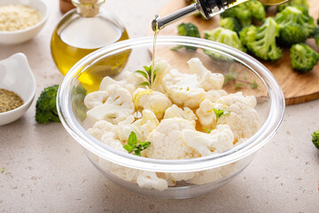 Raw cauliflower florets in a glass bowl, ready to roast with spices and olive oil pouring over - 755236364