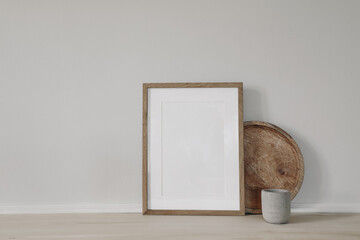 Blank vertical picture frame mockup. Poster display. Round wooden tray, concrete candleholder on working table, desk. Minimal rustic home. Scandinavian interior. White wall background. No people