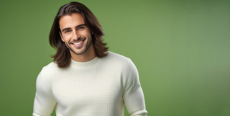 Young guy with dark hair, smiling broadly, white teeth, wearing white sweater. She poses on an isolated green background. Concept advertising businesses. Large portrait. Copy space.
