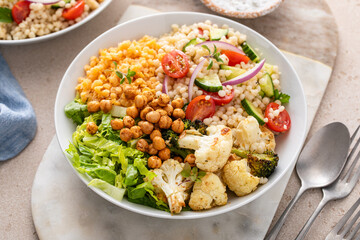 Vegan lunch bowl with roasted vegetables, fresh lettuce, cooked lentils, couscous salad and roasted chickpeas