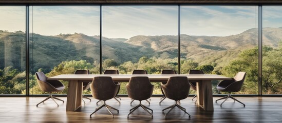 A conference room featuring minimalist chairs and a table on a hardwood floor, with a panoramic window offering a view of mountains in the countryside.