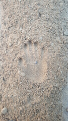 A hand is printed on sand of a beach. It looks like a hand print as we leave behind foot prints....