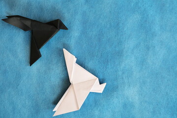 Black raven paper origami winning over a white dove. Good versus evil concept.