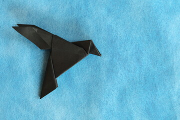 A black paper crow or raven origami isolated in blue background.