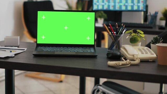 Focus on green screen laptop on office desk with computer in blurry background showing stock exchange data. Close up of mockup notebook and trading platform displayed on PC screen in the back