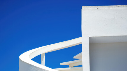 Architectural detail of a modern white building against a bright blue sky focusing on clean lines and geometric shapes